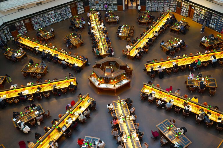 A vibrant scene of people studying in the iconic State Library of Victoria's reading room.