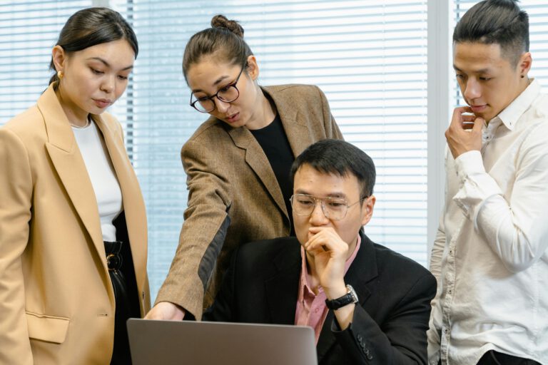 A group of focused professionals collaborating around a laptop in a modern office setting.